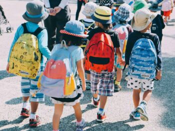 group of people wearing white and orange backpacks walking on gray concrete pavement during daytime